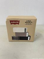 Front view of Levi's 3-pack web belts box showing beige, taupe, and dark brown belts with metal buckles.