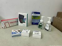 Wide view of all items in the lot on a white surface, including hand sanitizers, mouthpiece box, sterilization pouch, pill organizer, and three small white boxes.