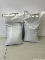 Two white woven seed bags side by side against a plain background