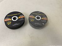 Two stacks of black circular cutting wheel discs for metal and stainless steel. One stack is wrapped in plastic, the other unwrapped showing normal condition.