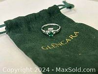 Photo of silver Claddagh ring with synthetic emerald heart-shaped stone on Glencara green dust bag, angled view