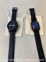 Two smart watches resting on beige cloth pouches, showing digital time displays.