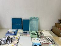 Photo of the lot displaying various new stationery items including multiple notebooks, file folders, exercise books, and pen sets spread on a flat surface.
