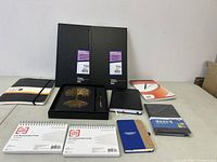 Photo shows assortment of stationary items including accounting books, notebooks, note cards, and journals arranged on a table.