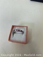 Sterling silver ring placed in a small pink jewelry box with white padding, showing front view of ring band and detailing.
