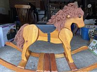 Side view showing entire wooden rocking horse with yarn mane and tail, leather saddle, and the curved rockers.