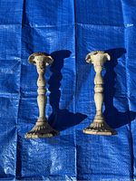 Full view of both cream colored cast iron candle sticks standing on blue tarp, showing height and form.