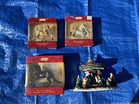 Front view of three horse ornaments in boxes and ceramic carousel figurine on blue backdrop