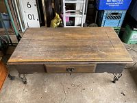 Top view of wooden coffee table showing worn wood surface, drawer with metal pull, and decorative metal legs.