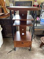 Front view of wood and metal entertainment stand showing three shelves, metal frame, and drawer with metal pull handle.