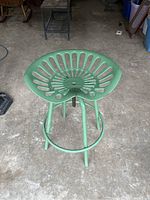 Full view of green tractor style stool showing perforated seat and tubular legs.