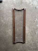 Rectangular metal grid pot holder frame with a brown metal border and a grid of cross rods, placed on a concrete floor.