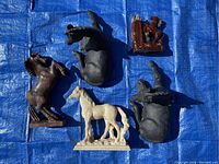 Top view of five horse figurines on blue tarp showing different horse figures including brown wooden horse, two black ceramic horses, white stone horse, brown ceramic horse base.