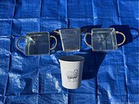 Top view of three silver metal square buckets with rope handles and one white round metal bucket with sheep illustration and metal and wood handle
