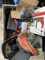 Top down photo showing a crate filled with various power and hand tools including a boxed drill, red leaf blower, and tool cases