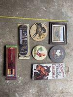 Top view showing all items including two packaged outdoor thermometers, three decorative circular plaques, one Christmas sign, and framed artwork.