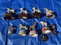 View of the back and bottoms of the carousel horse music boxes and other figurines, showing winding mechanisms and bases, some disconnected