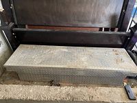 Top angled view of rectangular diamond plate metal truck bed box with surface rust and worn latch area.