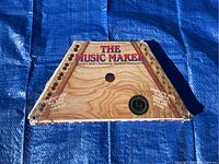 Top view of the stringed instrument showing its trapezoid wooden body with tuning pegs and strings, with text branding.