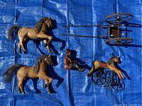 Overview of two wooden horses, jockey figure, metal cart, and metal/plastic horse figure on blue tarp