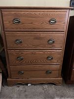Front view of the tall wooden chest of drawers showing four drawers with metal pulls and worn wood finish.