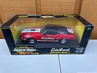 Front and side view of the boxed Edelbrock Mustang Mach 1 1:18 diecast model with visible white stripes and red paint.