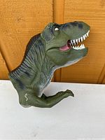 Front side of a green rubber T. Rex puppet with mouth open and detailed painted features.