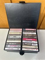 20 music cassette tapes organized in a black case showing visible artist names and labels.