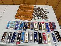 Full overview showing 26 souvenir spoons in packaging, many loose spoons, and three-tier wooden display rack on a table.