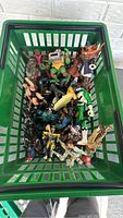 Green plastic storage bin filled with a variety of action figures including superheroes and fantasy characters, view from above.