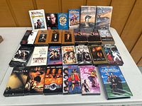 Photo showing the entire lot of VHS and BETA movie tapes on a table, arranged in rows. Caller includes 27 items in total including boxed Godfather sets and sealed Saving Private Ryan VHS tape.