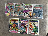 Photo showing all seven Marvel Iron Man comic books laid out on the floor, each individually bagged with visible colorful cover art depicting Iron Man in action and other characters.