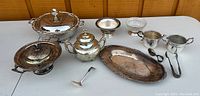 Wide view of silver serving set including teapot, creamer, sugar bowl, tray, covered dish and serving accessories on table.