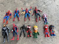 Overview of 12 assorted superhero figures laid out on concrete surface including multiple Spider-Man variants, Iron Man, and others.