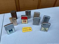 Photo of all nine lighters including advertising logo lighters and flint pack on table