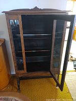 Front view of the antique china cabinet with one glass door open, showing the interior shelves and depth.
