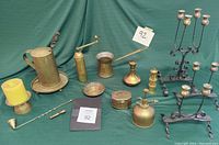 Overview of assorted brass and metal items displayed on green fabric, showing candlesticks, vase, coffee grinder, pot, tray, and others.