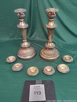 Photo of the complete set: two tall silver candlesticks alongside six small silver candleholders on green background.