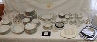 Full overview of white and silver china set on table showing plates, bowls, cups, serving platters, and additional pieces.
