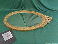 Full view of the oval mirror on a green cloth, showing the ornate wood frame and overall shape and size.