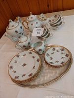 Porcelain red rose floral tea set including teapot, sugar pot, creamer, cups, saucers, plates, warming pot and tray arranged on table.