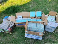 Three boxes of tiles outside on grass showing different types and sizes of ceramic tiles.