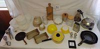 Overview of vintage kitchen lot showing Pyrex bowls, yellow cookware, cast iron pans, kitchen tools and jars.