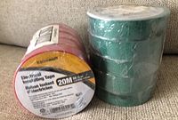 Photo showing 5 rolls of green electrical tape stacked together wrapped in plastic, and 5 rolls of red electrical tape with visible label showing 20 meters length