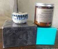Four new candles including a Friendo Apothecary jar, small blue patterned tin candle, turquoise square candle, and sealed black box candle.