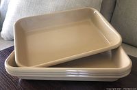 Four stacked beige rectangular enamelled trays on a wooden table with a couch in background.