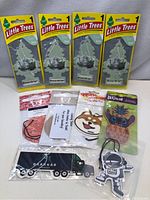 Photo shows a lot of 10 air fresheners, including 4 Little Trees brand 'Midnight Black Ice' in sealed packaging, plus six other novelty or branded air fresheners in sealed packaging, all new.