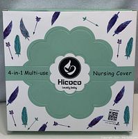 Front of box showing Hicoco 4-in-1 Multi-use Nursing Cover with feather and arrow pattern and logo in center.