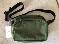Front view of dark green Baggu fanny pack showing the main compartment and a smaller front compartment with black adjustable strap and plastic buckle.