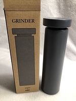 Photo of the HAY salt or pepper grinder next to its original packaging box, showing the box labeled 'GRINDER' and the sleek, cylindrical black grinder.